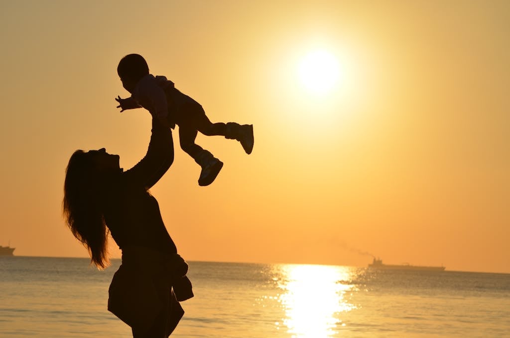 Silhouette of a mother lifting her child at a sunset beach, capturing warmth and love. Mother's Day Gift