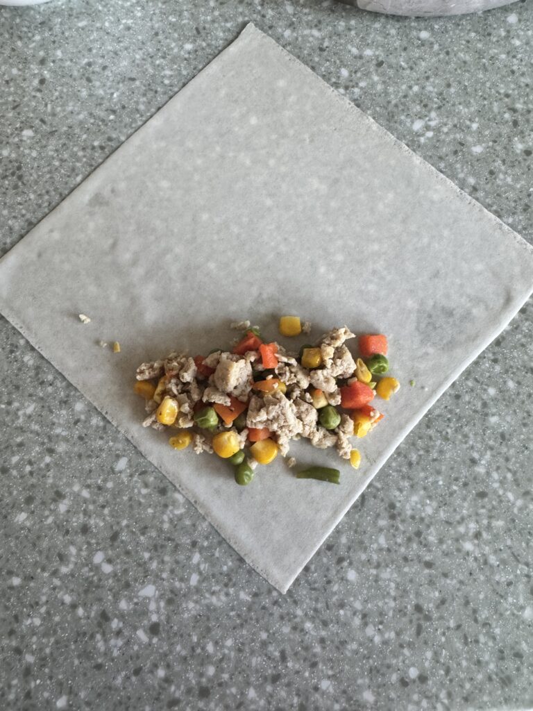 chicken and veggie laid on the bottom corner of an egg roll wrapper