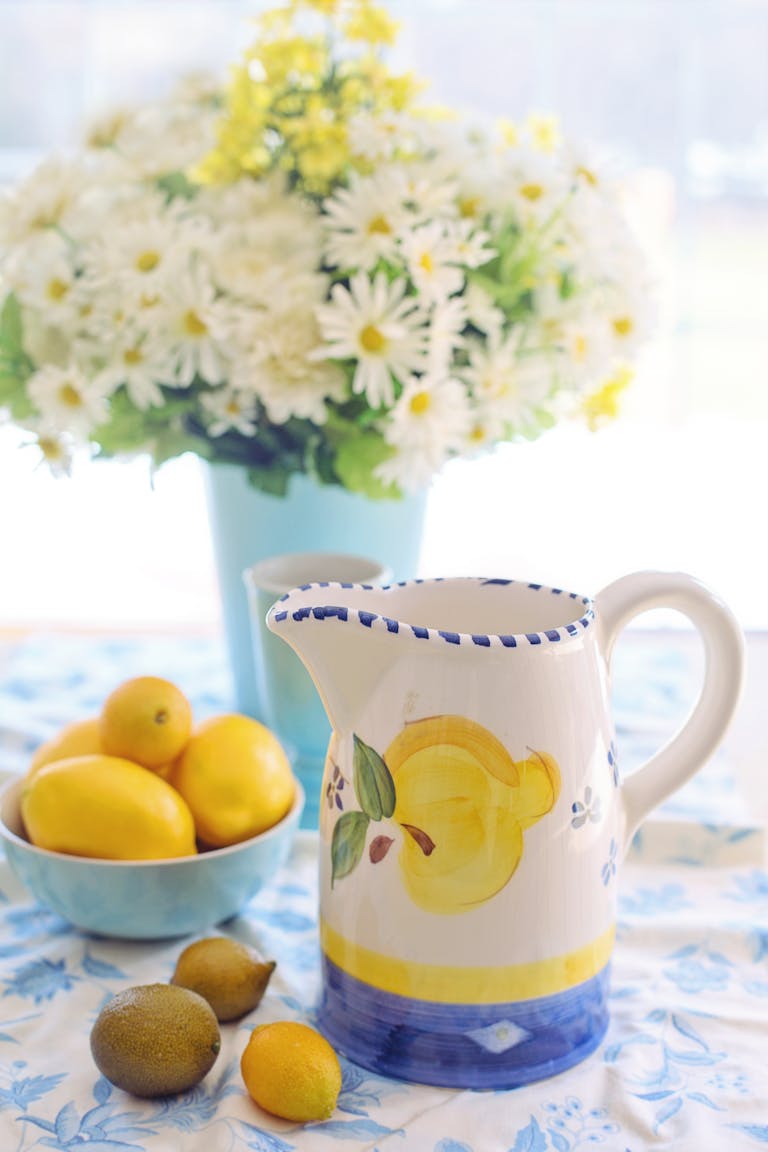 Vibrant lemon-themed table setting featuring a ceramic pitcher and daisy bouquet. Cute summer hostess gift