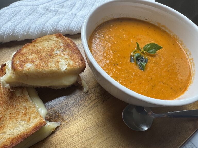 Roasted tomato soup with crispy grilled cheese on a platter, perfect for a cozy fall meal.